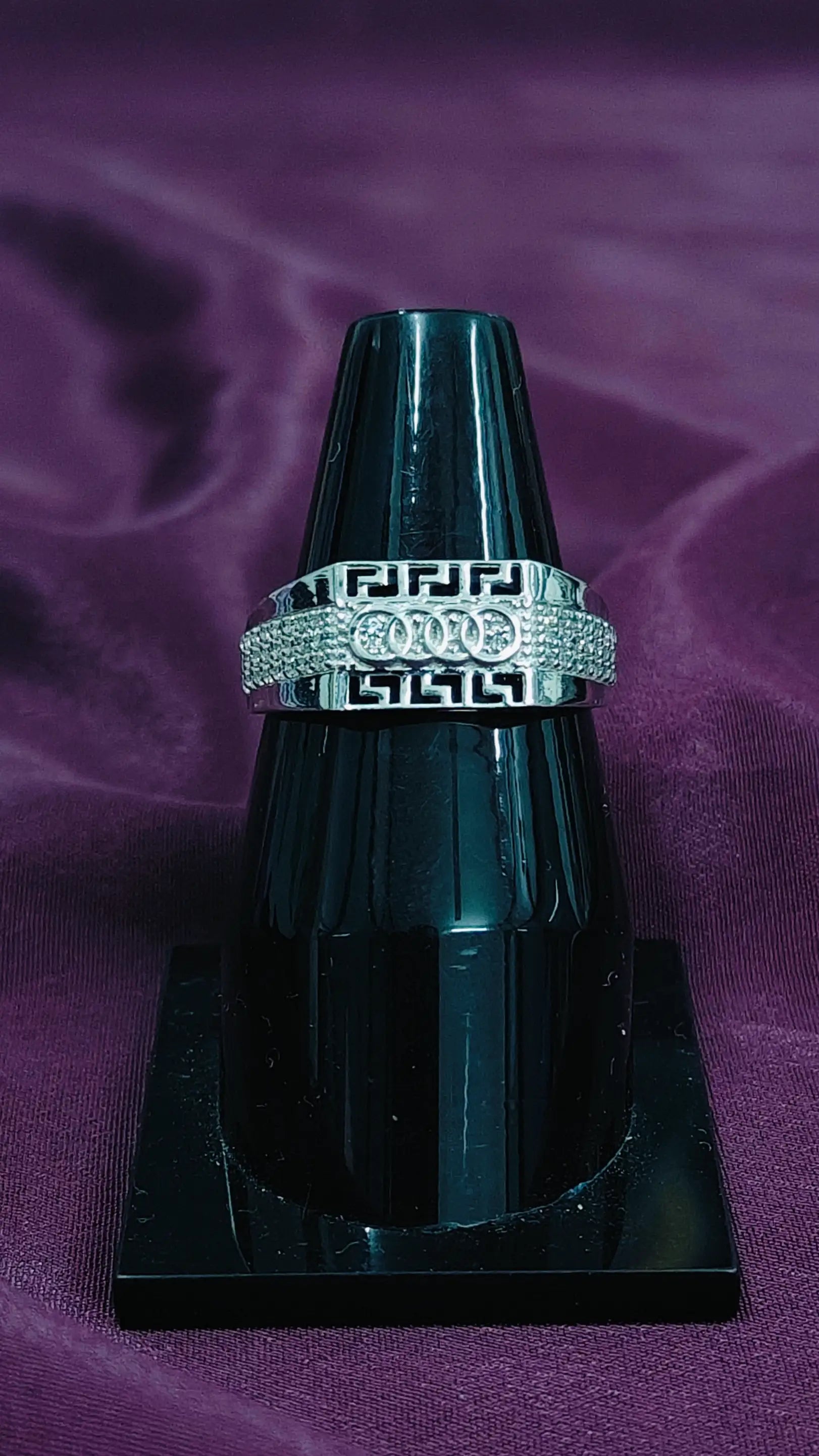 Silver ring with a diamond band on a black stand against a purple background